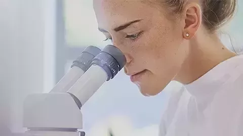 Ein Wissenschaftler im Laborkittel untersucht aufmerksam eine Probe unter dem Mikroskop.