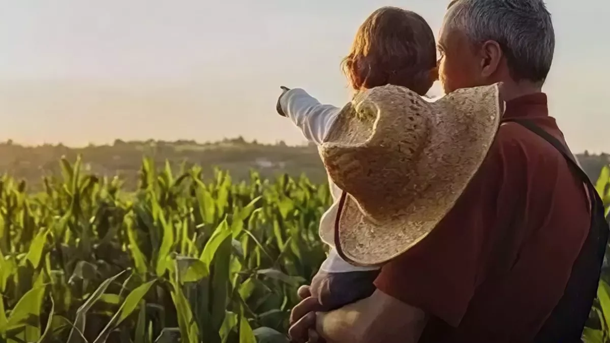 Person mit einem Kind auf dem Arm schaut in ein Feld